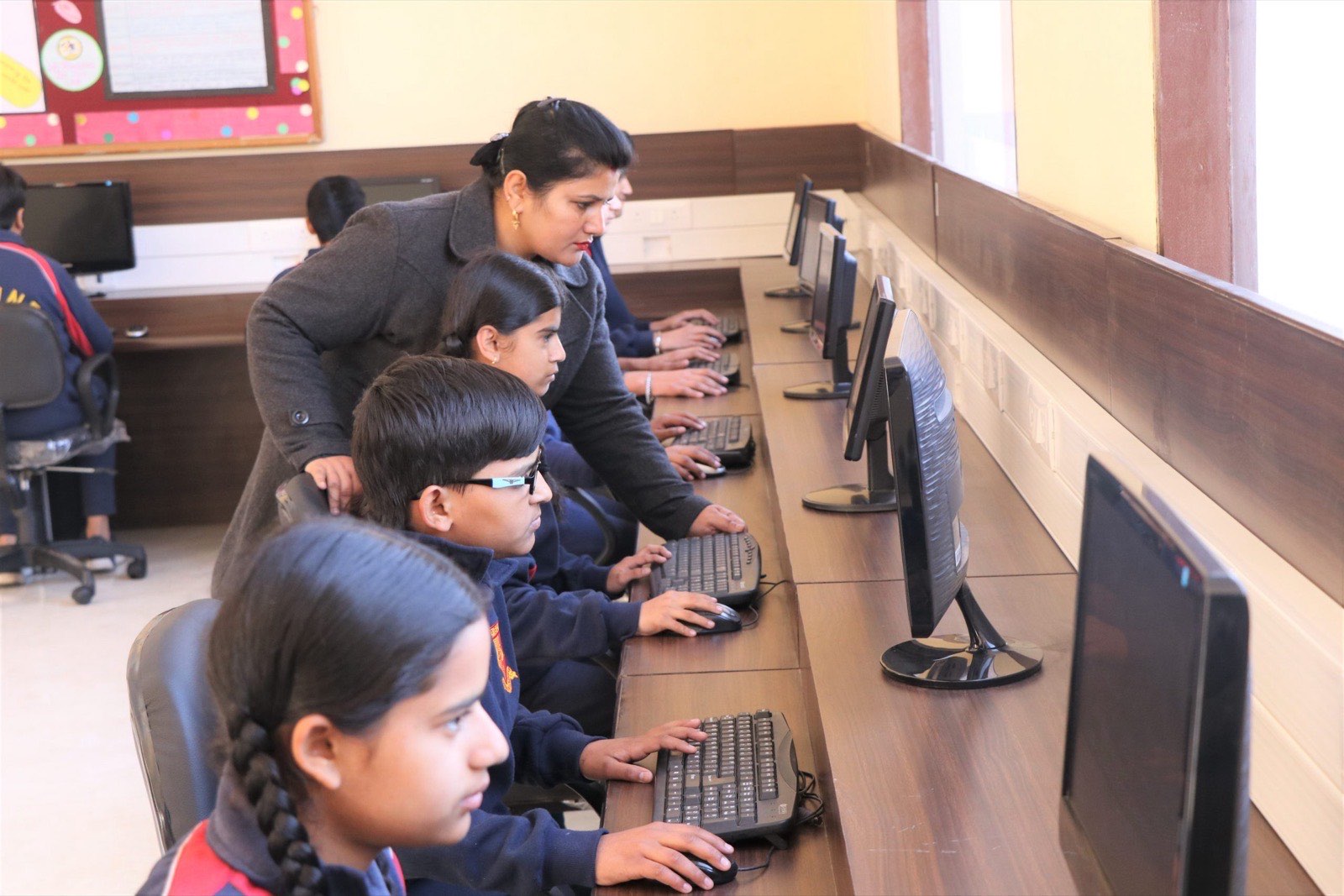 A teacher guiding students working at computers in the computer laboratory